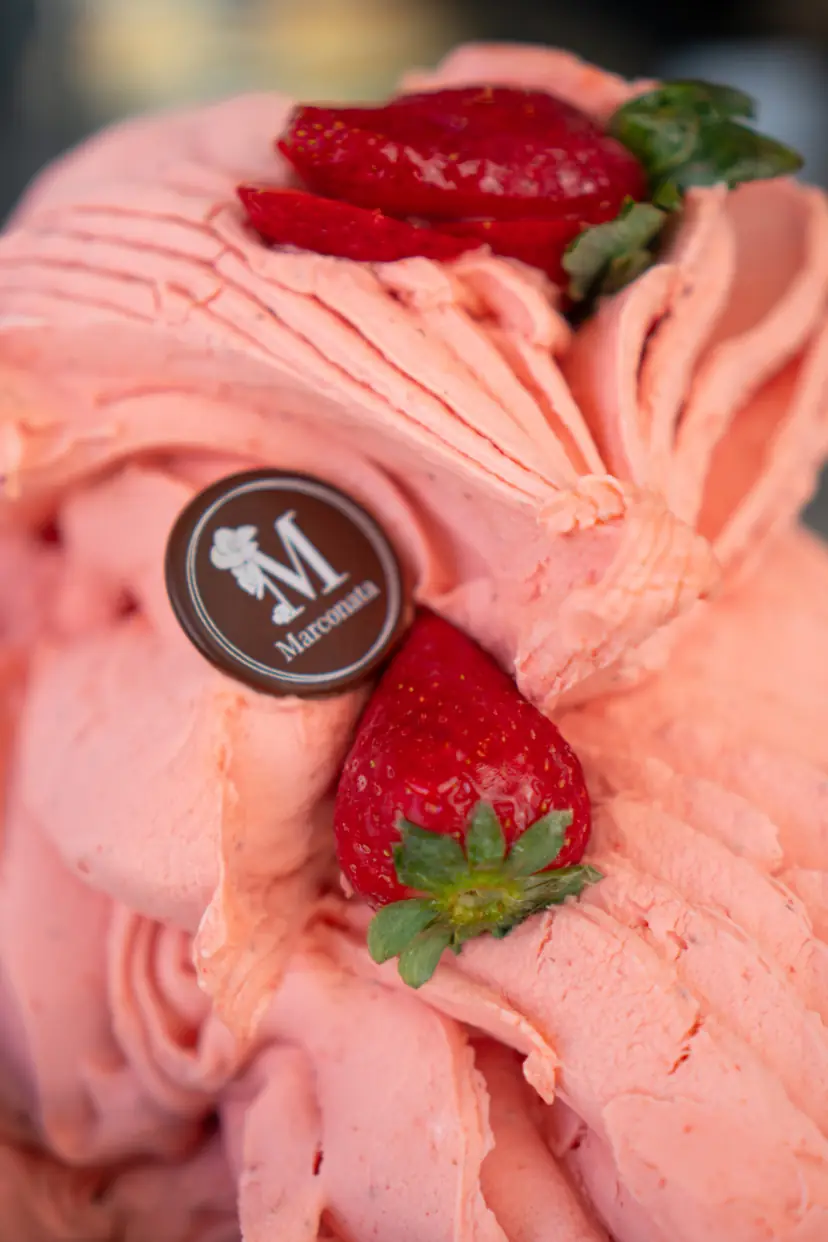Helado rosa con fresas enteras por encima y una placa de chocolate con la M de Marconata