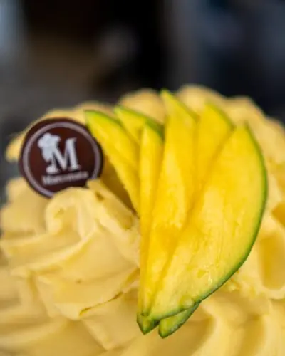 Helado amarillo con láminas de mango por encima y una placa de chocolate con la M de Marconata