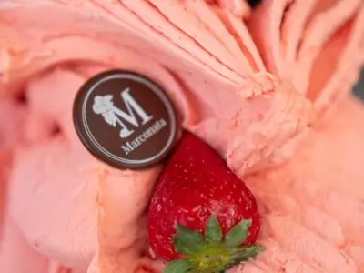 Helado rosa con fresas enteras por encima y una placa de chocolate con la M de Marconata